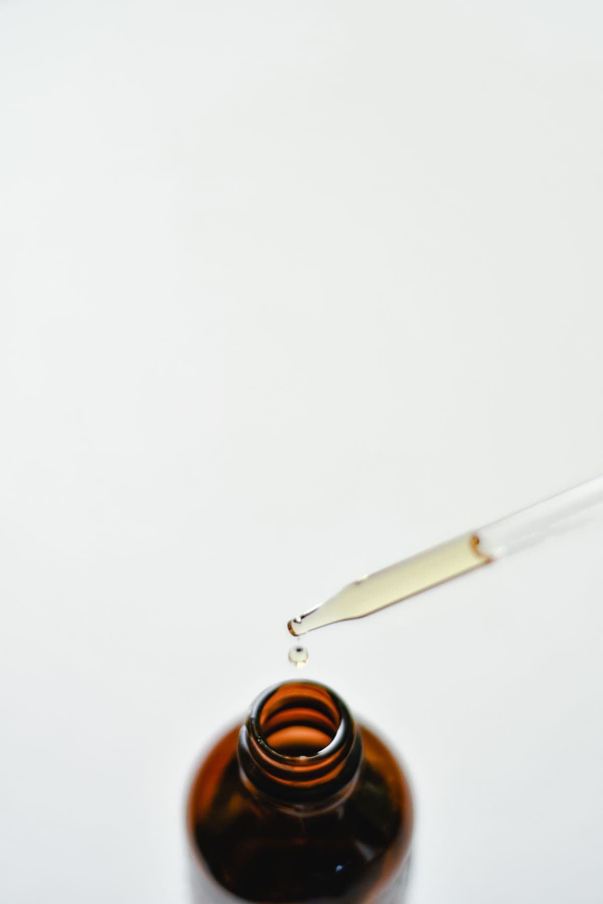 A pipette dispensing a drop of golden oil into the bottle
